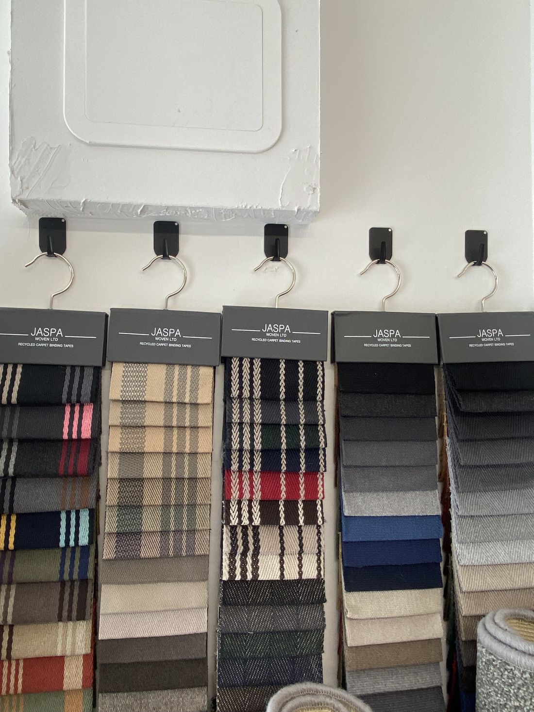 Jaspa woven sample books hanging in the Wiltshire Rugs studio, showing tape and binding options